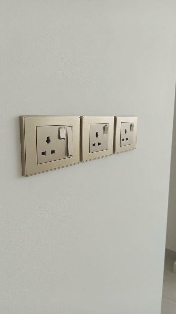 Three brushed gold switched sockets on a white wall