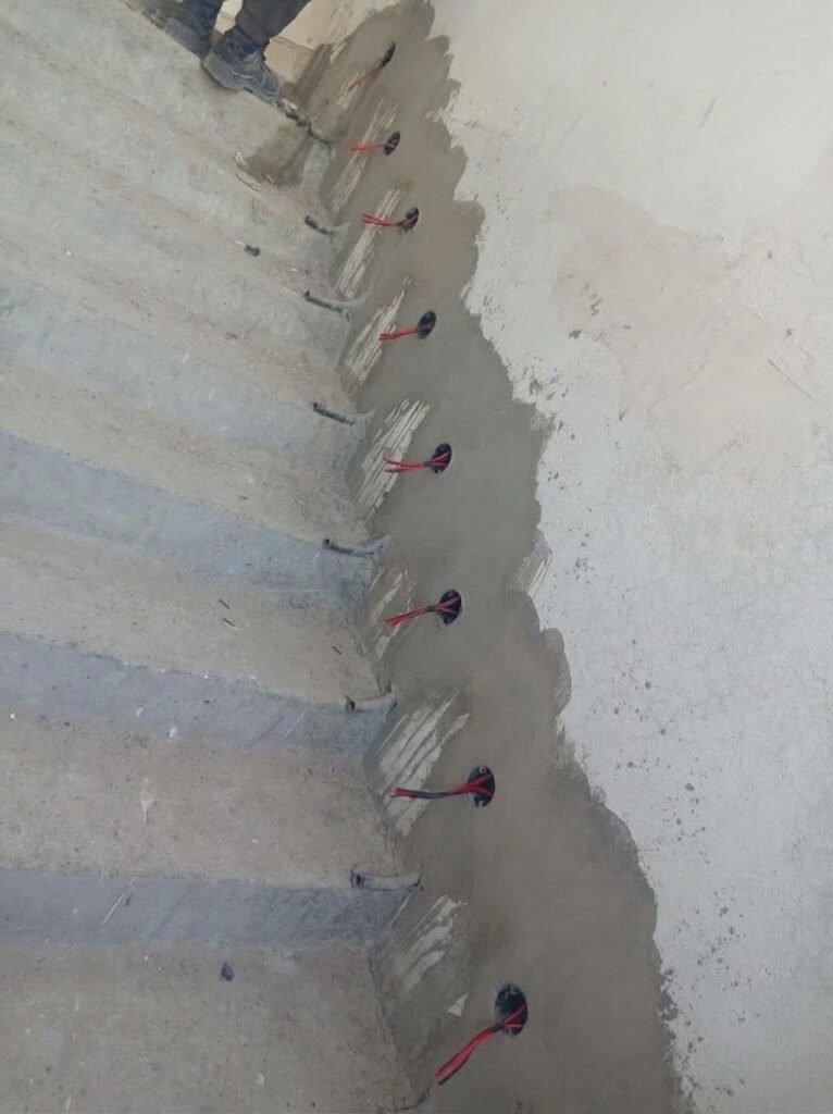 Row of light point boxes with red cables along a concrete staircase wall